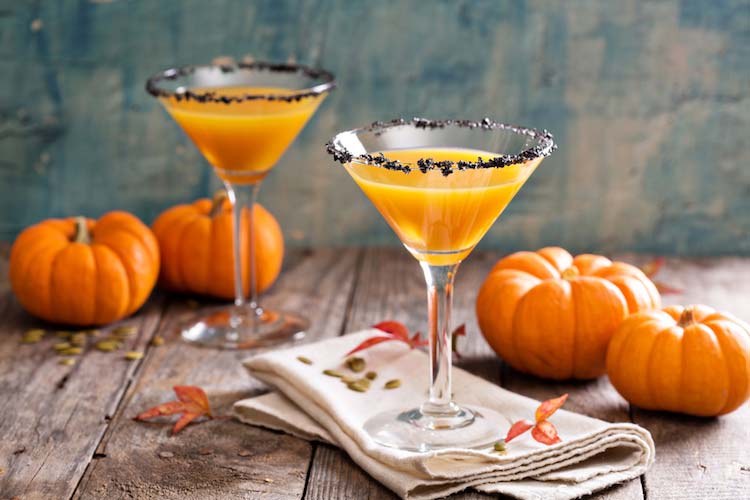 two Halloween cocktails with small pumpkins on a farm table